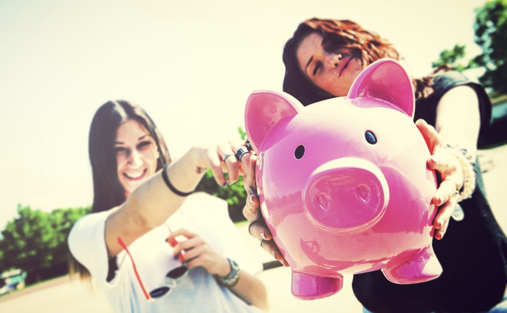 Two young funny woman holding piggy bank talking about Cost of LASIK