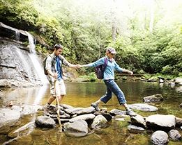 Young couple crossing rocks in the water while looking at map and holding compass with waterfall in the background