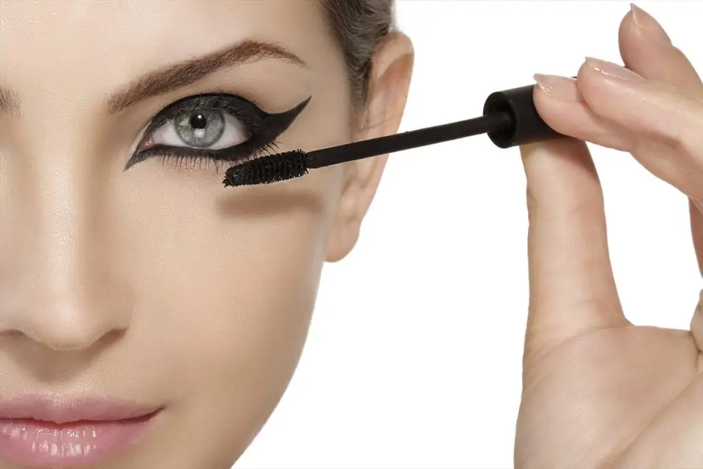 Beautiful model applying eye makeup and mascara on eyelashes close up on white