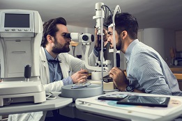 Male ophthalmologist examining young man's eyesight with optical instrument